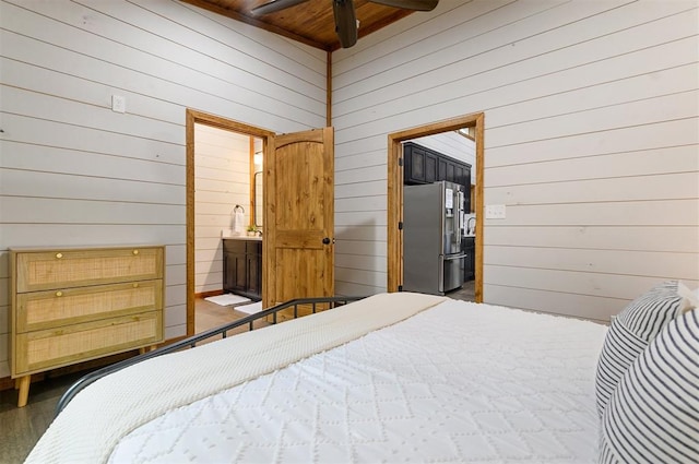 bedroom featuring stainless steel fridge, connected bathroom, dark wood-type flooring, and wood walls