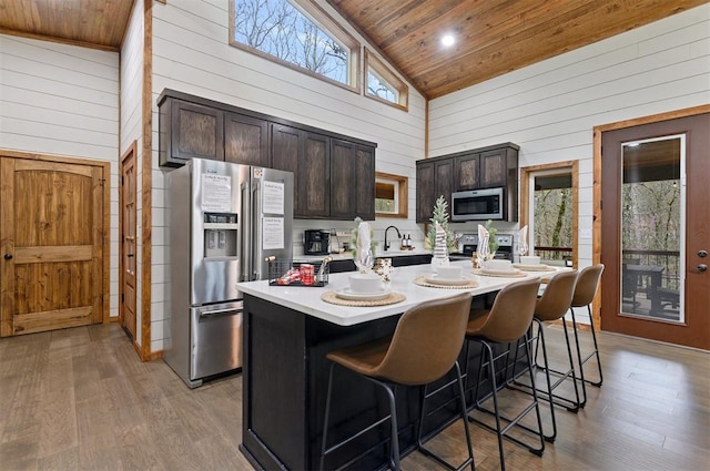 kitchen with appliances with stainless steel finishes, high vaulted ceiling, dark brown cabinets, and an island with sink