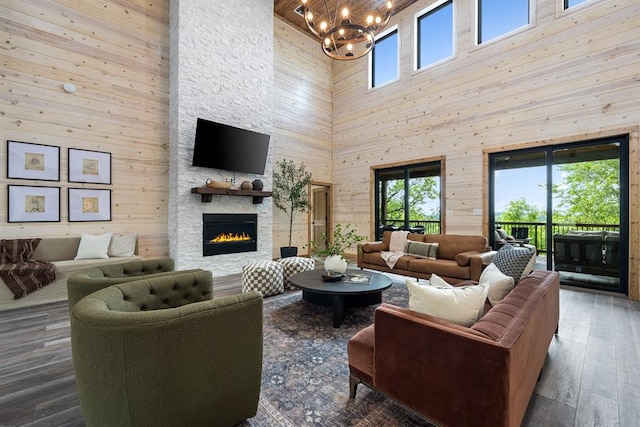 living room with an inviting chandelier, wooden walls, a towering ceiling, a fireplace, and wood-type flooring