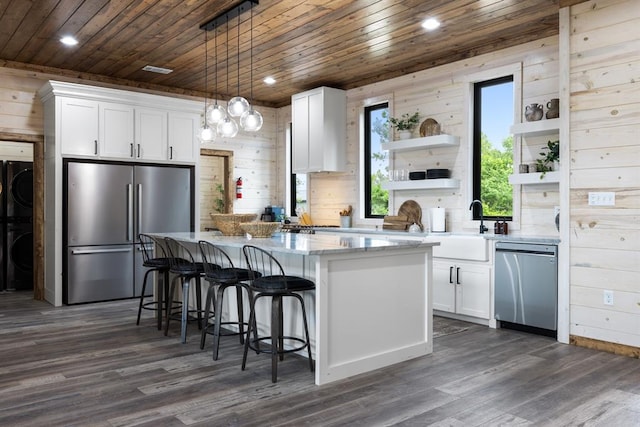 kitchen with wood walls, pendant lighting, white cabinets, and stainless steel appliances