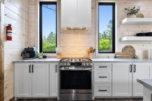 kitchen with white cabinets, stainless steel range with gas cooktop, dark wood-type flooring, and wooden walls