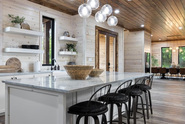 kitchen featuring light wood-type flooring, white cabinetry, light stone counters, and wooden walls