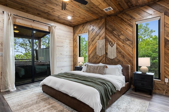 bedroom featuring access to exterior, hardwood / wood-style flooring, multiple windows, and wood walls