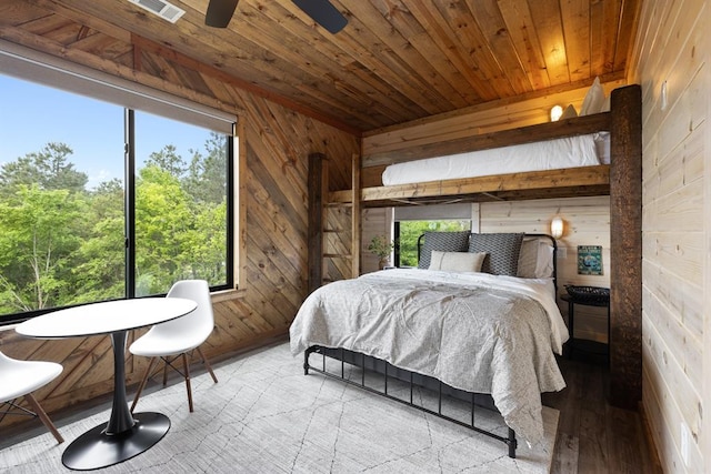 bedroom featuring light hardwood / wood-style floors, wooden walls, and multiple windows