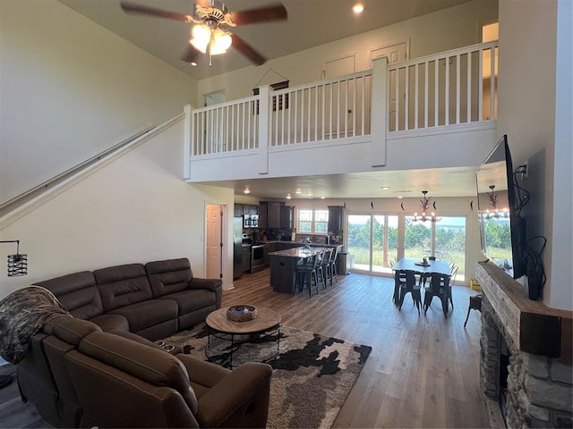 living room featuring hardwood / wood-style floors, ceiling fan with notable chandelier, and a towering ceiling