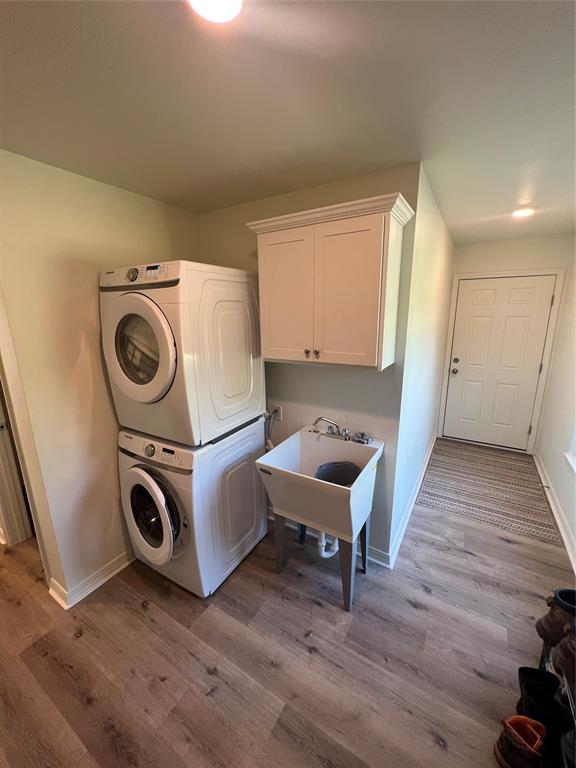 laundry area with cabinets, stacked washer and dryer, light hardwood / wood-style floors, and sink