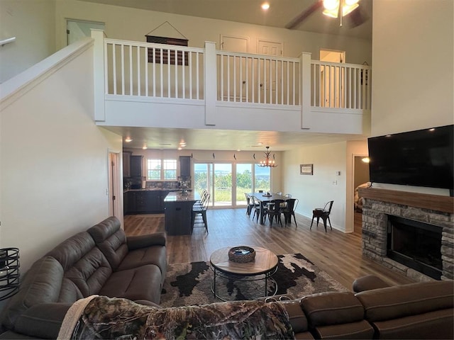 living room featuring ceiling fan with notable chandelier, hardwood / wood-style floors, a towering ceiling, and a fireplace