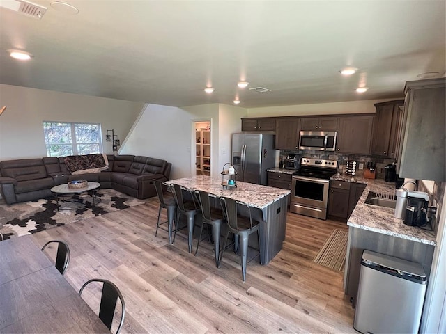 kitchen with light stone countertops, a kitchen island, light hardwood / wood-style floors, and appliances with stainless steel finishes