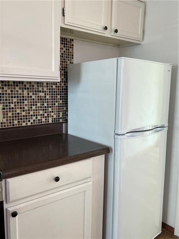 kitchen with white cabinets, white refrigerator, and tasteful backsplash