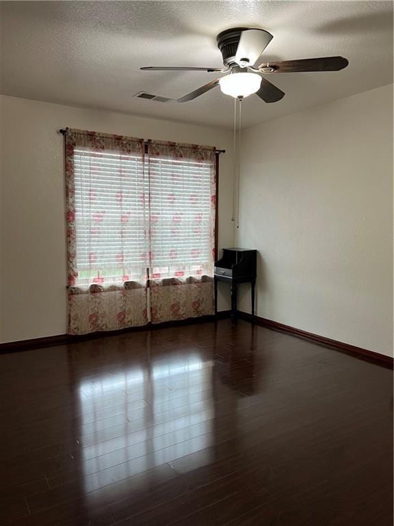 empty room with a textured ceiling, ceiling fan, and dark wood-type flooring