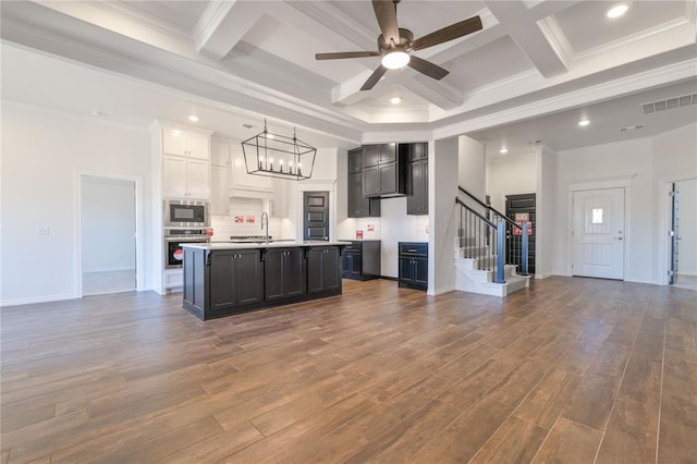 kitchen with stainless steel oven, built in microwave, crown molding, a center island with sink, and white cabinetry