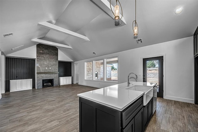 kitchen featuring sink, hanging light fixtures, a kitchen island with sink, a fireplace, and hardwood / wood-style flooring