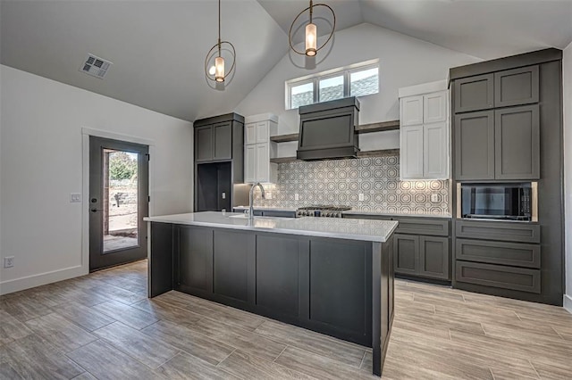 kitchen with gray cabinetry, backsplash, a center island with sink, sink, and hanging light fixtures