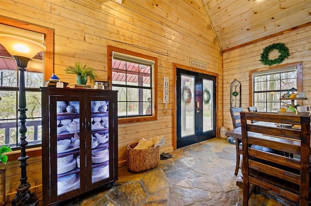 entryway featuring french doors, high vaulted ceiling, plenty of natural light, and wood walls