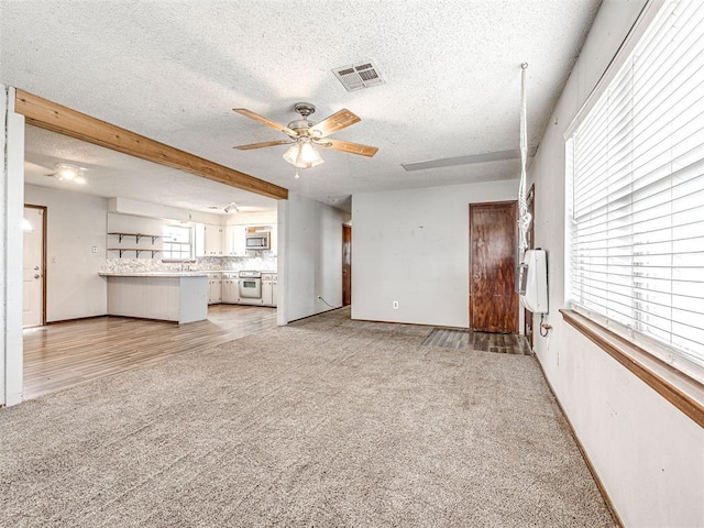 unfurnished living room with a textured ceiling, light colored carpet, and ceiling fan