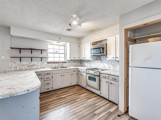 kitchen with sink, decorative backsplash, a textured ceiling, appliances with stainless steel finishes, and light hardwood / wood-style floors