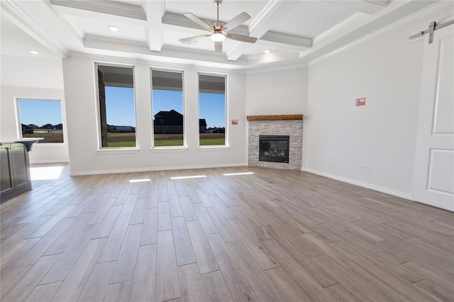 unfurnished living room featuring ceiling fan, a barn door, beamed ceiling, crown molding, and light wood-type flooring