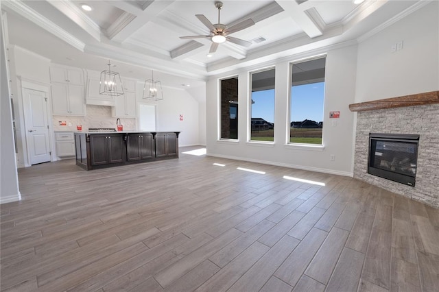 unfurnished living room with light hardwood / wood-style floors, a stone fireplace, crown molding, and coffered ceiling