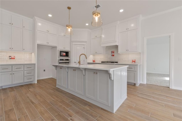 kitchen featuring a center island with sink, oven, hanging light fixtures, light hardwood / wood-style flooring, and black microwave