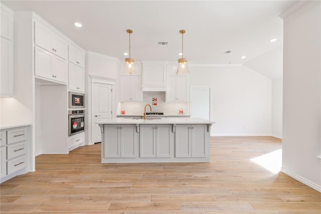 kitchen with pendant lighting, a center island with sink, white cabinetry, and stainless steel appliances