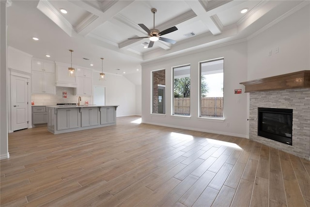 unfurnished living room featuring coffered ceiling, a stone fireplace, crown molding, light wood-type flooring, and beamed ceiling