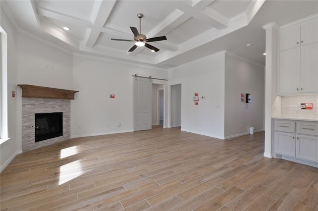 unfurnished living room featuring coffered ceiling, a barn door, ornamental molding, light wood-type flooring, and a fireplace