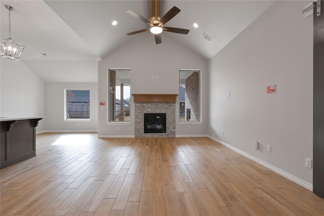 unfurnished living room featuring a stone fireplace, light hardwood / wood-style flooring, high vaulted ceiling, and ceiling fan with notable chandelier