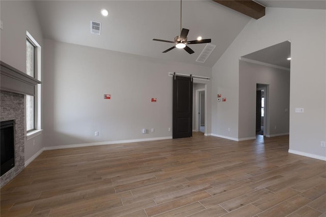 unfurnished living room with a barn door, high vaulted ceiling, light hardwood / wood-style flooring, beamed ceiling, and a stone fireplace