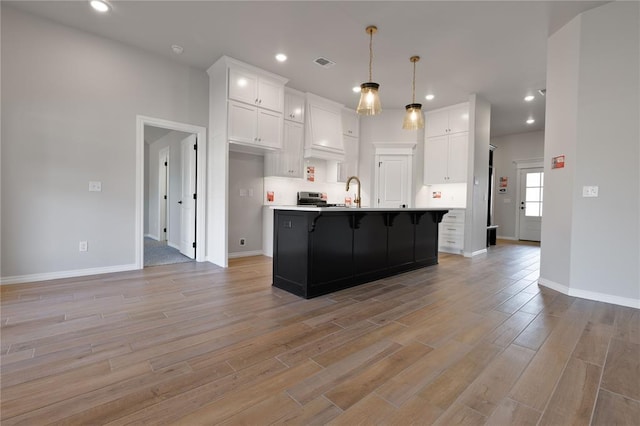 kitchen with decorative light fixtures, light hardwood / wood-style floors, white cabinetry, and a kitchen island with sink