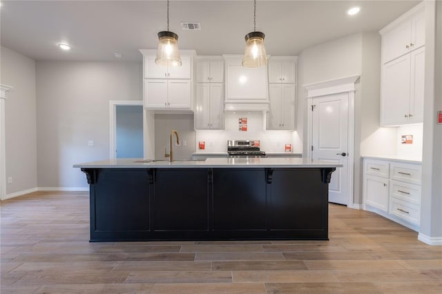 kitchen with white cabinetry, sink, stainless steel stove, and a center island with sink