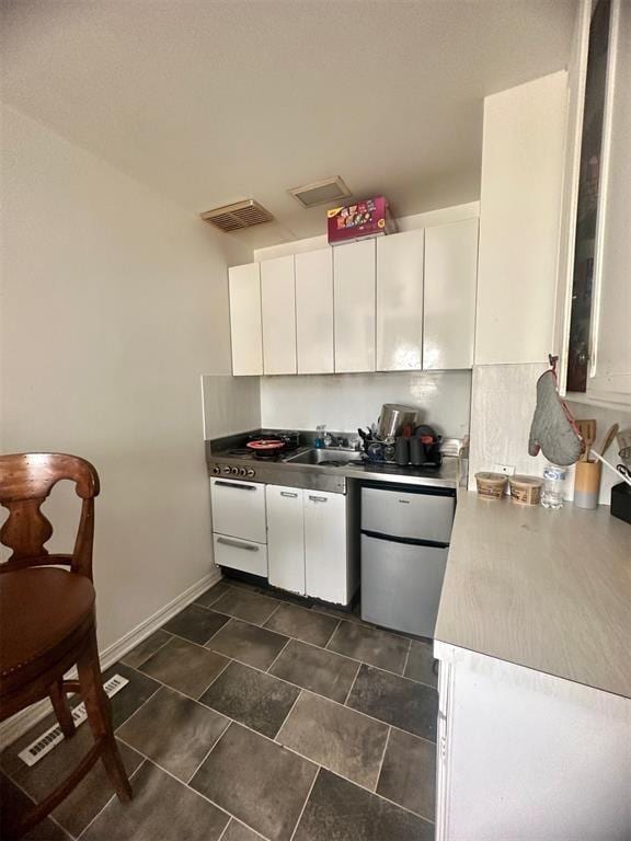 kitchen with stainless steel fridge, white cabinetry, and sink