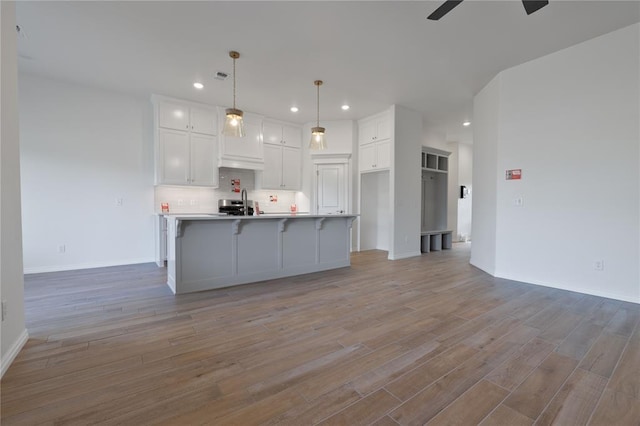 kitchen featuring a kitchen island with sink, white cabinets, light hardwood / wood-style floors, and decorative light fixtures