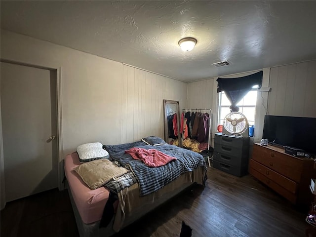 bedroom featuring dark hardwood / wood-style flooring, a textured ceiling, and wooden walls