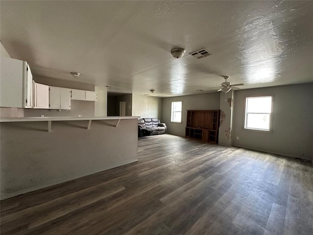 unfurnished living room featuring ceiling fan, dark wood-style flooring, visible vents, and a healthy amount of sunlight