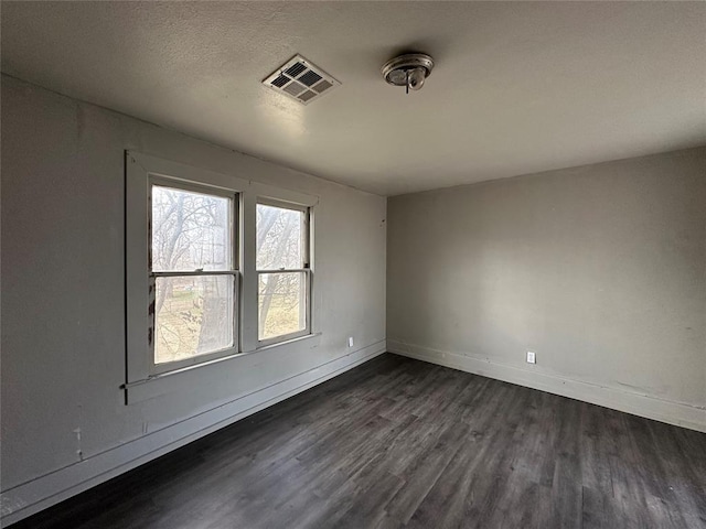 unfurnished room with dark wood-type flooring, visible vents, a textured ceiling, and baseboards