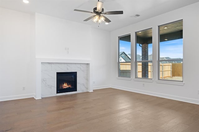 unfurnished living room with ceiling fan, wood-type flooring, and a tiled fireplace