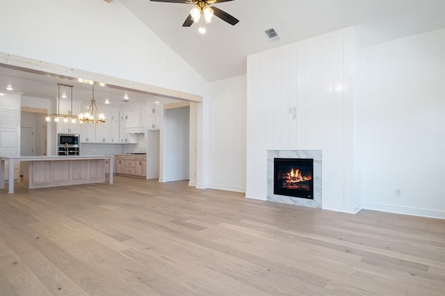 unfurnished living room featuring ceiling fan, a high end fireplace, high vaulted ceiling, and light wood-type flooring