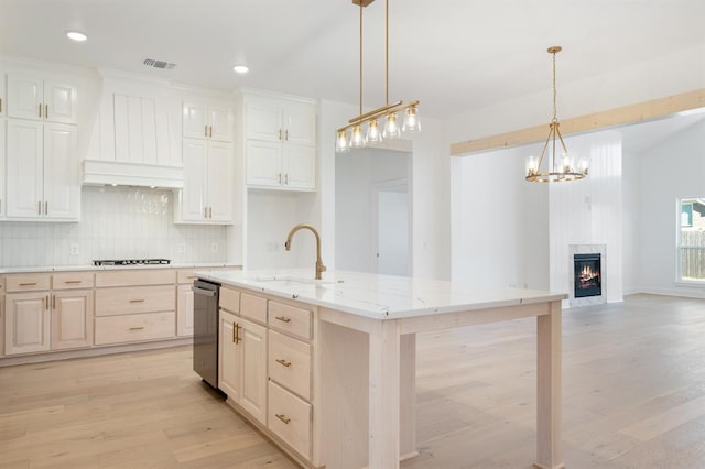 kitchen with sink, hanging light fixtures, premium range hood, light hardwood / wood-style floors, and a kitchen island with sink