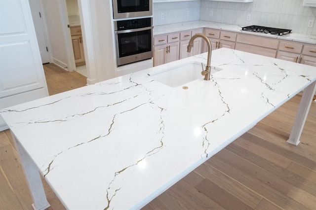 kitchen featuring light stone counters, an island with sink, light brown cabinetry, appliances with stainless steel finishes, and light wood-type flooring