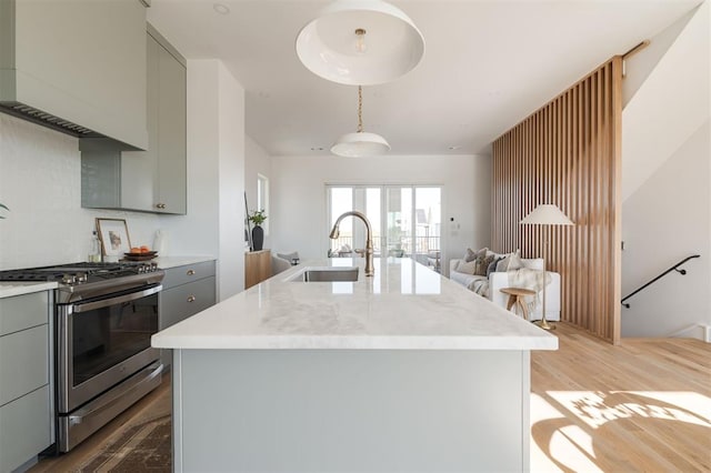 kitchen featuring stainless steel gas stove, gray cabinets, a center island with sink, and light hardwood / wood-style floors