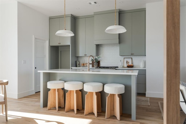 kitchen with sink, light hardwood / wood-style flooring, an island with sink, and tasteful backsplash