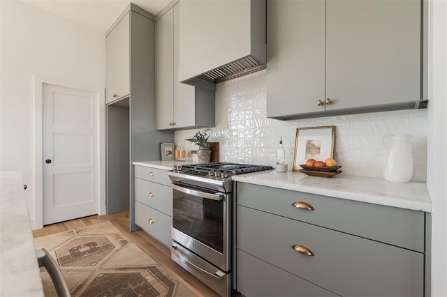 kitchen featuring gray cabinetry, decorative backsplash, light wood-type flooring, and stainless steel range with gas stovetop