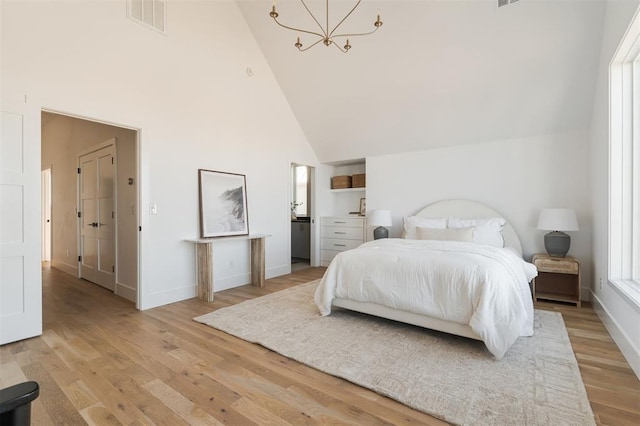 bedroom featuring light hardwood / wood-style floors, high vaulted ceiling, and an inviting chandelier