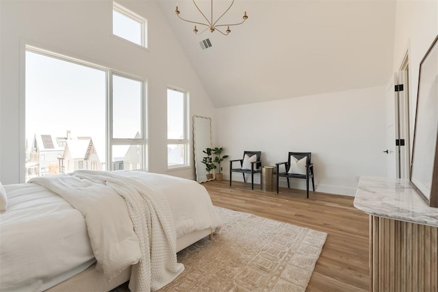 bedroom with multiple windows, an inviting chandelier, high vaulted ceiling, and light wood-type flooring