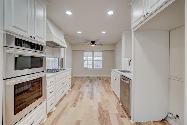 kitchen featuring white cabinets, light hardwood / wood-style flooring, ceiling fan, appliances with stainless steel finishes, and custom range hood