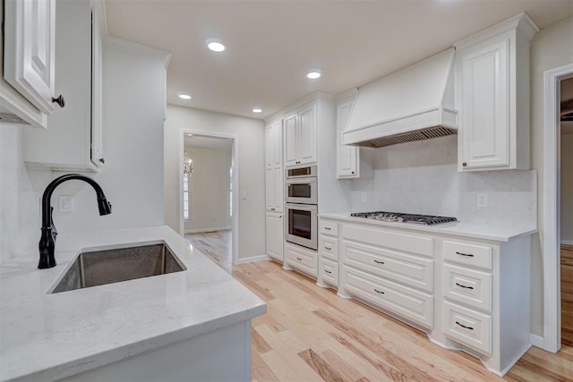 kitchen with sink, stainless steel appliances, white cabinets, custom range hood, and light wood-type flooring