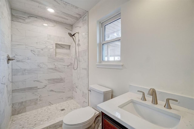 bathroom featuring a tile shower, vanity, and toilet