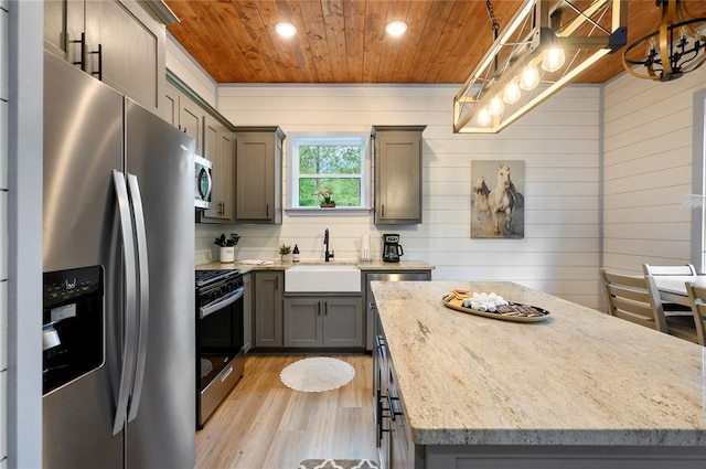 kitchen with light stone countertops, appliances with stainless steel finishes, sink, light hardwood / wood-style floors, and hanging light fixtures