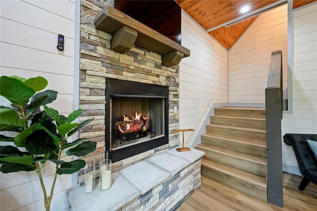 stairway featuring wooden ceiling, wood finished floors, vaulted ceiling, wood walls, and an outdoor stone fireplace