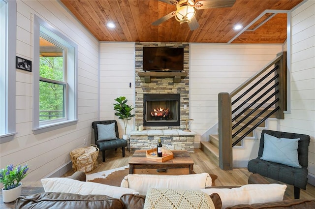 living room featuring ceiling fan, wood walls, a stone fireplace, and light hardwood / wood-style flooring